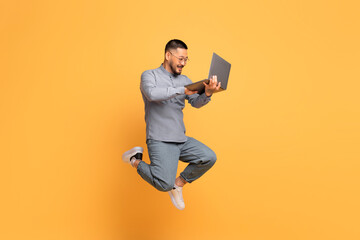Online Offer. Happy Young Asian Man With Laptop Jumping Over Yellow Background
