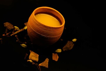 Close up of Indian masala tea in clay pot on black background. Refreshing morning tea with cardamon