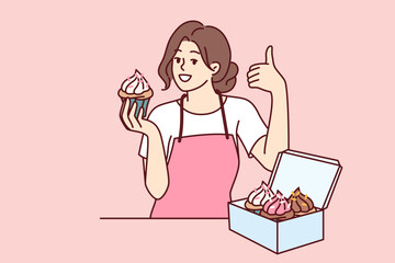 Woman pastry chef holding cupcake and showing thumb up, standing near box of muffins or desserts. Buttercream cupcake in hands of girl who works in bakery and invites visitors to try sweet cakes.