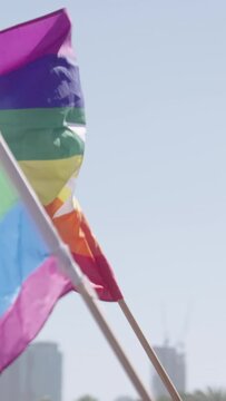 Vertical video slow motion of the rainbow flag waving during a pride parade in a city streets