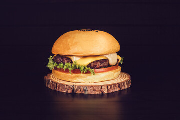 Close-up of a homemade tasty single beef burger on wooden piece on a dramatic black background