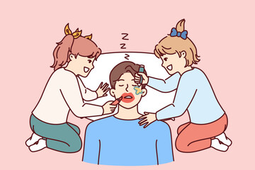 Funny little girls make up sleeping father by painting on man face with lipstick and colored markers. Two cheerful preteen daughters play pranks and laugh father sleeps after work.