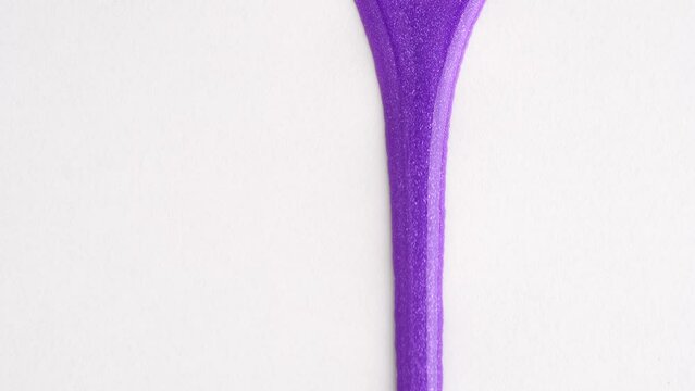 Liquid drops of bright shiny purple paint flowing on the white surface. Purple nail polish. Sample of makeup in lavender color