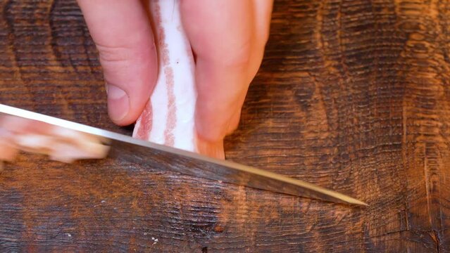 Slicing of salted pork fatback on cutting board, close-up. Ukrainian traditional food - salo