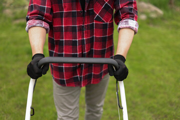 Cropped photo of professional male gardener is trimming and caring green grass lawn pushing modern electric cordless lawnmower at backyard of house. Landscaping industry theme.