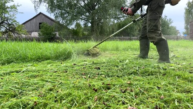 Gardener mows weeds grass. Man cutting grass in yard by using string trimmer. Worker lawn mower cutting garden. Lawn mowing machine. Grass Trimmer and Grass Cutter. lawn maintenance service.