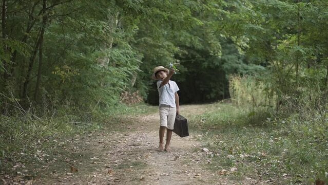 Boy in the forest walking towards the camera carrying a suitcase and playing with a toy airplane. Child using his imagination outdoors. Vintage style look.