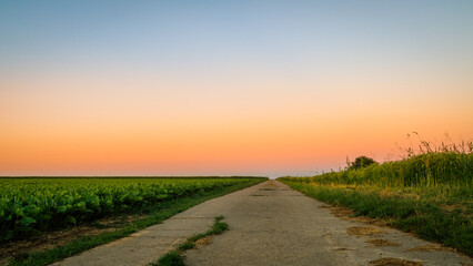 Obraz premium Beautiful view of the road during the sunset and green meadows in two sides