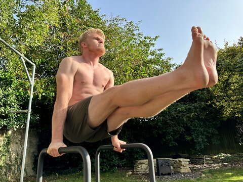 Low angle shot of a shirtless athletic man doing leg raises on parallel bars