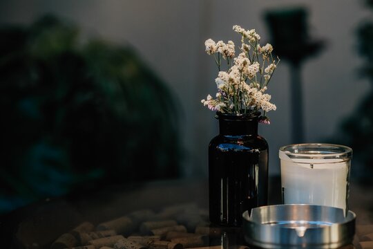 Wooden table with white flowers in a black vase, a candle and an ashtray
