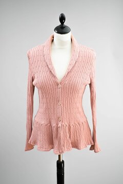 A beautiful rose pink blouse top hangs on a headless mannequin against a light gray background.