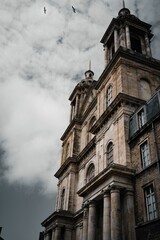 Fototapeta premium Grand old church with birds flying around it on the background of the cloudy sky