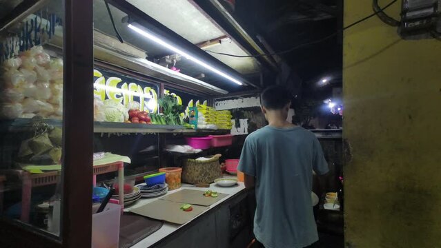 Jakarta, Indonesia - September 21, 2023: Javanese noodle seller with his cart preparing the meal for customer. Traditional Indonesian street food seller.