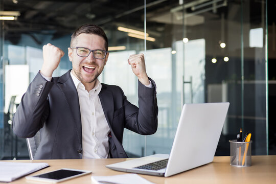 Portrait of a happy young businessman sitting at a desk in the office and celebrating success at work