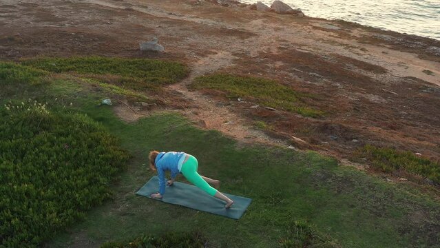 Senior woman doing hatha yoga ocean background at sunset. Pensioner woman making relaxing asana outdoors. Healthy senior lifestyle. Self care concept. Aerial view