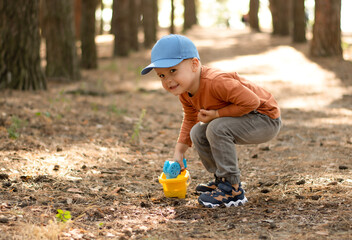 Children. A small handsome and emotional boy in a blue cap and a red jacket plays with soap bubbles in the fresh air in the forest.