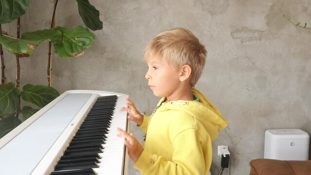 Cute child, boy, playing piano at home, learning how to play music