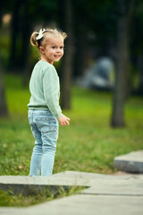 Beautiful, cute, happy little girl walking in park on warm autumn day having foot time outdoors. Positive emotions