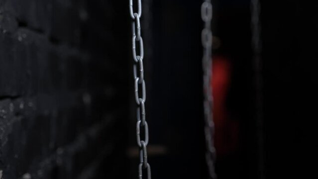 Close-up of hanging metal chains in a dark room, chains swinging from side to side. Quest room or horror room.