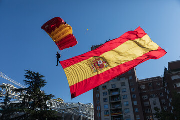 Vista de un paracaidista aterrizando en el paseo de la Castellana llevando una gran bandera de España el día de la fiesta nacional, Madrid, España.