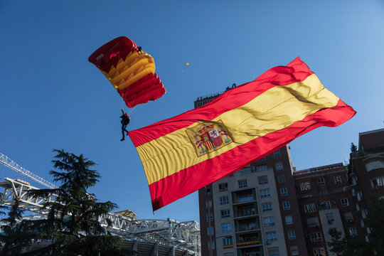 Vista de un paracaidista aterrizando en el paseo de la Castellana llevando una gran bandera de Espa&ntilde;a el d&iacute;a de la fiesta nacional, Madrid, Espa&ntilde;a.
