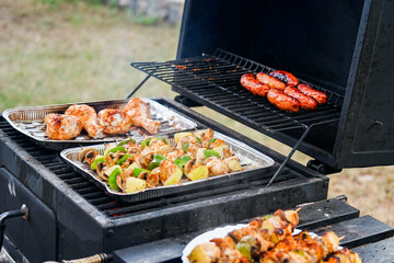 Grilling some meat, sausages and vegetable skewers on a charcoal Stove, He is cooking for BBQ Party with Friends in the garden
