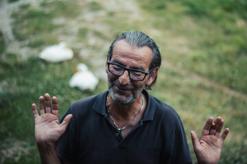 Amidst nature's beauty, a lively Serbian senior, 60 years young, with glasses and flowing hair, finds joy in animated conversations while sporting a contagious smile