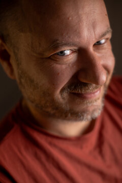 An unshaved man in his 40s, sporting a friendly smile and an average appearance, is captured in a close-up shot