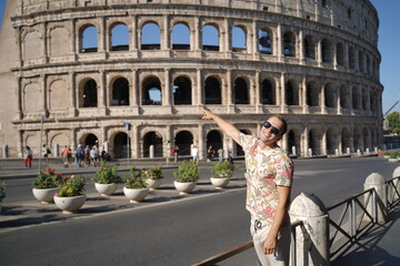 A young man wearing glasses points to the Colosseum in Italy. Vacation.