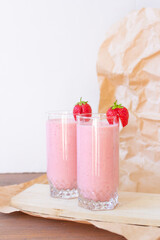 Strawberry fresh pink berry smoothie on wooden table and craft paper, vertical photo, two glasses of juice 