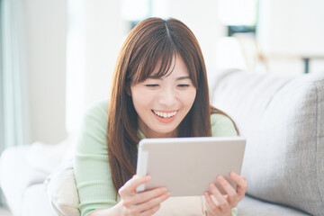 リビングのソファに横になってタブレットを見ながらくつろぐ女性
