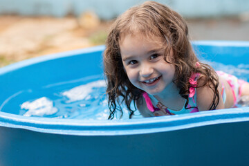 Uma criança se refrescando na piscina azul de plástico.