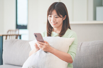 リビングのソファに座ってスマートフォンを操作しながらくつろぐ女性