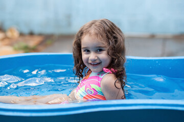 Fototapeta na wymiar Uma criança se refrescando na piscina azul de plástico.