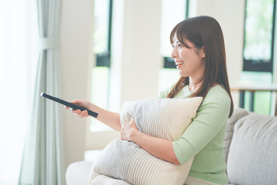 リビングのソファに座ってテレビのリモコンを操作する女性