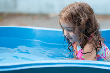 Uma criança se refrescando na piscina azul de plástico.