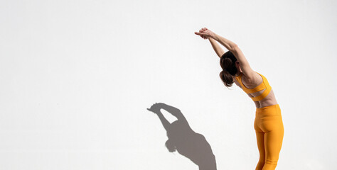Female athlete doing backbend pose by a white wall