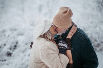 Elegant senior couple kissing in the snowy park, during cold winter snowy day.