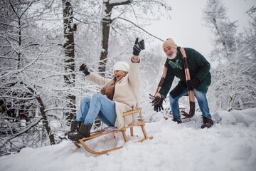 Senior couple having fun during cold winter day, sledding down the hill.