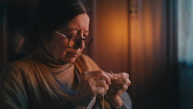 Elderly woman in eyeglasses knitting close-up hobby at senior age, motor control