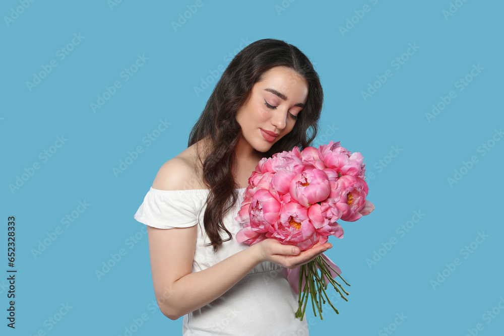 Wall mural Beautiful young woman with bouquet of pink peonies on light blue background