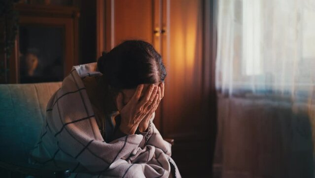 Depressed senior woman crying alone in room, sitting in armchair, loneliness