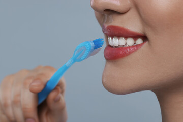 Woman brushing her teeth with plastic toothbrush on light grey background, closeup