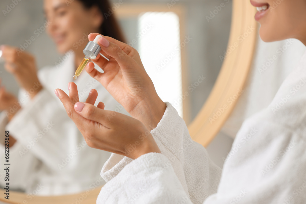 Wall mural Young woman applying cosmetic serum onto her hand indoors, closeup