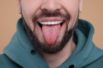 Obraz na płótnie Canvas Happy man showing his tongue on beige background, closeup