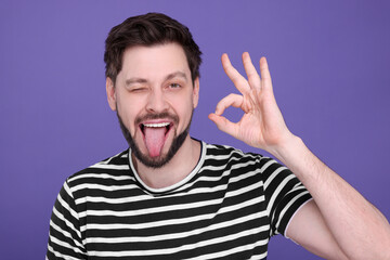 Happy man showing his tongue and making ok gesture on purple background