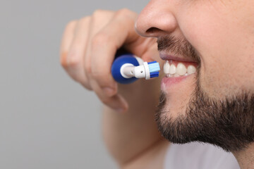 Man brushing his teeth with electric toothbrush on light grey background, closeup. Space for text