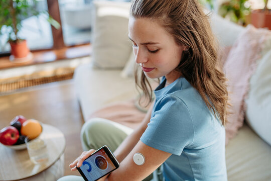 Woman with diabetes checking blood glucose level at home using continuous glucose monitor.