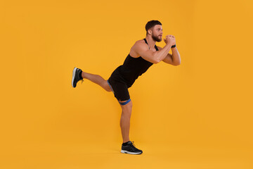 Fototapeta na wymiar Young man exercising with elastic resistance band on orange background