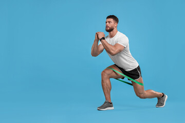 Fototapeta na wymiar Young man exercising with elastic resistance band on light blue background. Space for text